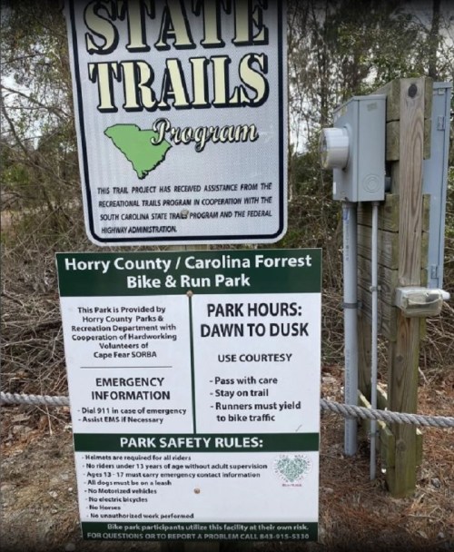 Sign for Horry County/Carolina Forest Bike & Run Park with park hours, emergency info, and safety rules.