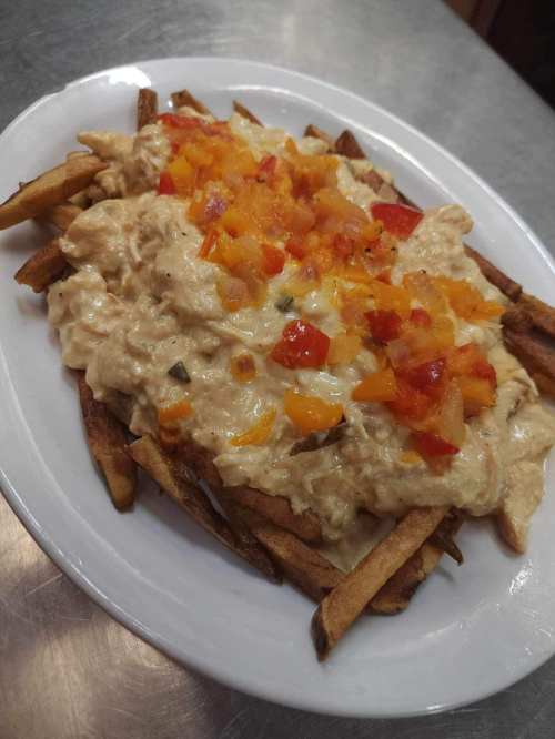 A plate of fries topped with creamy sauce and diced tomatoes.