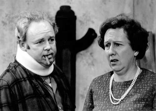 A man in a neck brace with a cigar looks concerned, while a woman in a pearl necklace appears distressed.