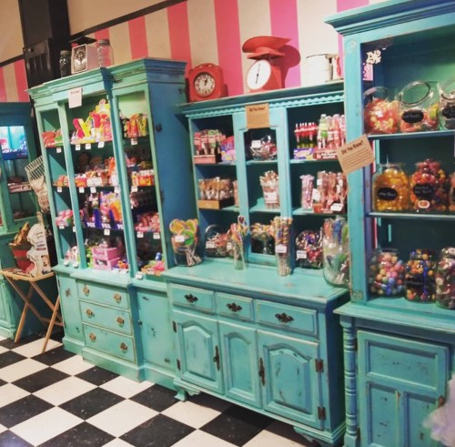Colorful candy shop display with turquoise cabinets filled with various candies and treats against a striped pink wall.