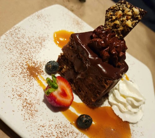 A decadent chocolate cake topped with whipped cream, a chocolate garnish, and fresh berries on a white plate.