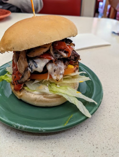 A delicious sandwich with grilled meat, roasted peppers, lettuce, tomato, and sauce, served on a soft bun.