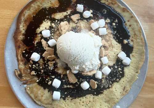 A large pancake topped with chocolate sauce, crushed graham crackers, mini marshmallows, and a scoop of vanilla ice cream.