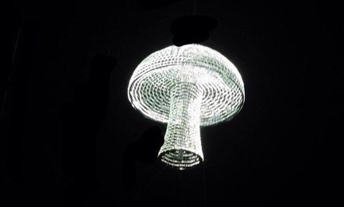 A glowing chandelier shaped like a mushroom, illuminated against a dark background.