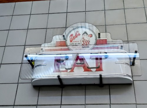 Sign reading "EAT" with a vintage diner logo above it, mounted on a tiled wall.