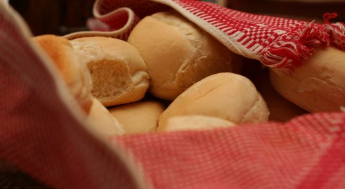 A basket of freshly baked bread rolls wrapped in a red and white checkered cloth.