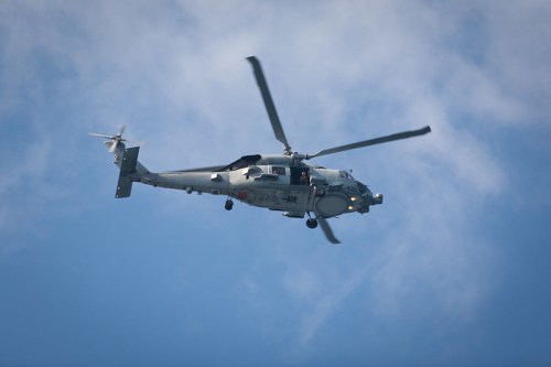 A military helicopter flying against a blue sky with scattered clouds.