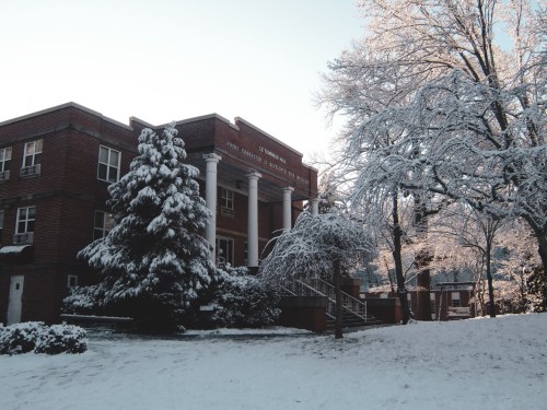 A brick building surrounded by snow-covered trees and a snowy landscape, creating a serene winter scene.