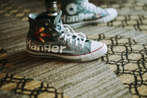 Colorful high-top sneakers with "Hanger" painted on the side, resting on a patterned carpet.
