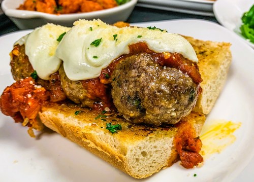 A close-up of meatballs topped with marinara sauce and melted cheese on toasted bread, garnished with parsley.