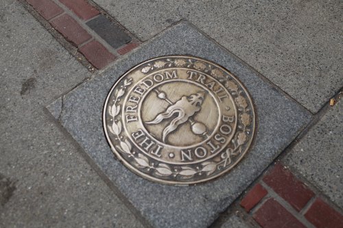 A bronze medallion embedded in pavement, marking the Freedom Trail in Boston.