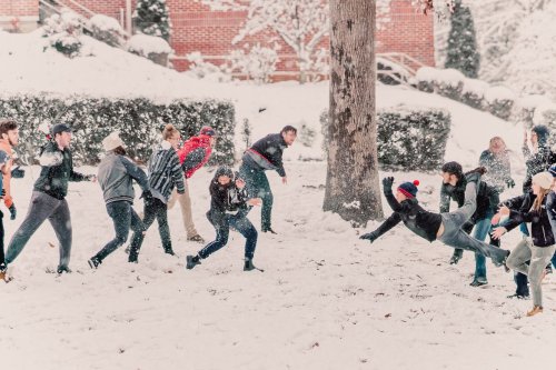 A group of people play in the snow, throwing snowballs and enjoying a winter day in a park.