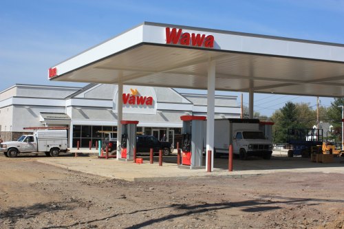 A Wawa gas station with a convenience store, featuring fuel pumps and parked vehicles in a construction area.
