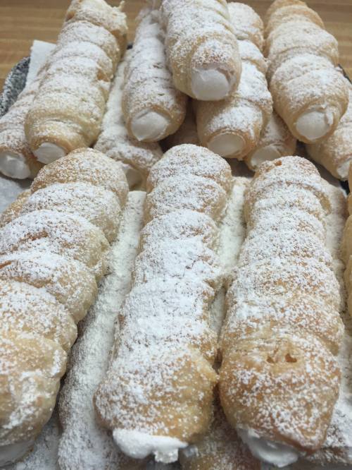 A close-up of multiple cream-filled pastries dusted with powdered sugar, arranged neatly on a tray.