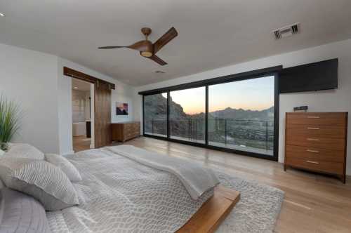 Modern bedroom with a wooden bed, large windows showcasing a mountain view, and stylish furniture.