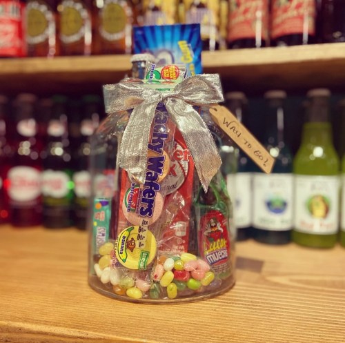 A glass jar filled with colorful candies and snacks, tied with a silver ribbon and a tag that says "Way to Go!"