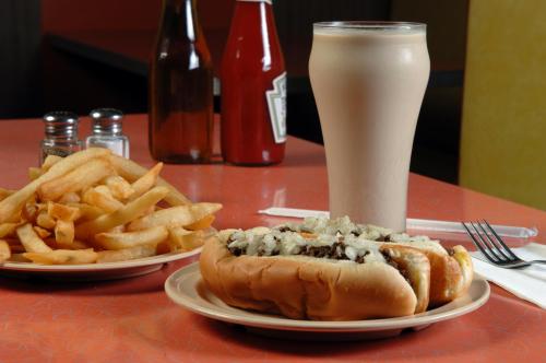 A plate with a hot dog topped with onions, a side of fries, and a tall glass of a creamy beverage on a diner table.