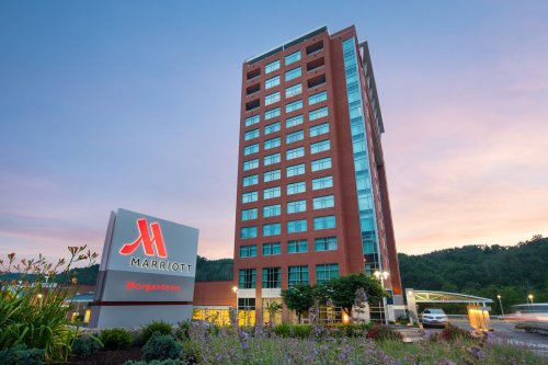 Marriott hotel in Morgantown at dusk, featuring a tall building and illuminated sign amidst landscaped flowers.