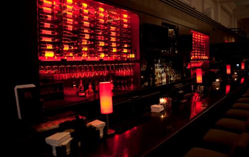 A dimly lit bar with red lighting, showcasing a wall of wine bottles and a sleek counter with glowing lamps.