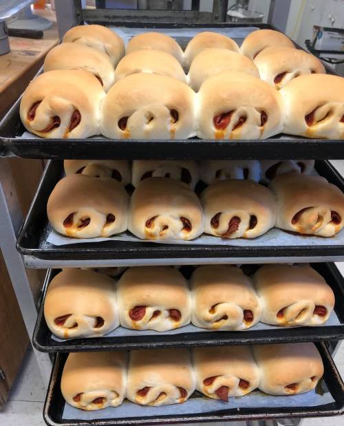 Freshly baked rolls on trays, golden brown and fluffy, with visible fillings peeking out.