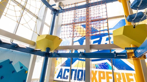 Indoor adventure course featuring climbing structures and a colorful action-themed backdrop.
