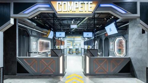 A modern competition arena with sleek design, featuring screens and barriers, under a sign that reads "COMPETE."