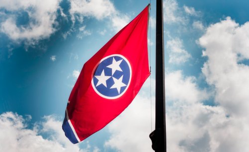 Tennessee state flag waving against a blue sky with clouds.