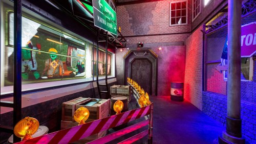 A colorful indoor space resembling a construction zone, with barriers, lights, and a window showing animated characters.