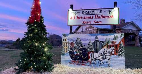 A festive scene featuring a decorated tree and a sign for "A Christmas Hallmark Movie Town" at sunset.