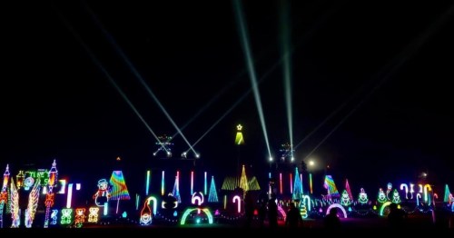 A vibrant display of colorful lights and decorations at night, with beams of light illuminating the scene.