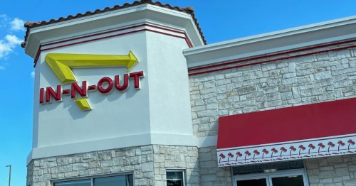 Signage of an In-N-Out restaurant featuring a yellow arrow and red lettering against a stone building.