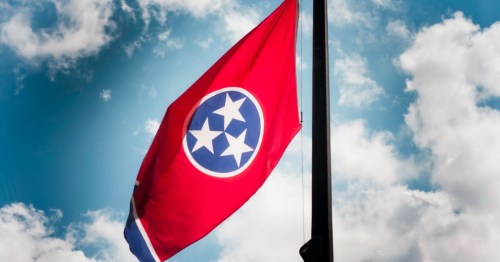 Tennessee state flag waving against a blue sky with clouds.