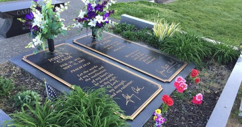 Two gravestones adorned with flowers, surrounded by greenery, in a peaceful cemetery setting.