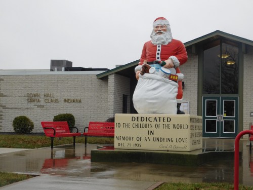 A large Santa Claus statue stands in front of the Town Hall in Santa Claus, Indiana, on a rainy day.