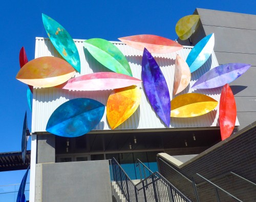 Colorful, abstract leaf-shaped sculptures adorn a modern building against a clear blue sky.
