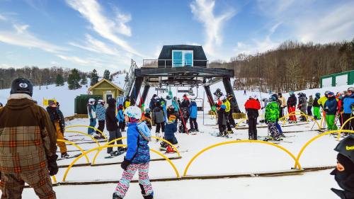 A busy ski resort scene with skiers waiting in line at a ski lift on a snowy day.