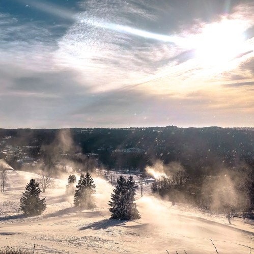 A snowy landscape with trees and mist, under a bright sky with clouds and sunlight.