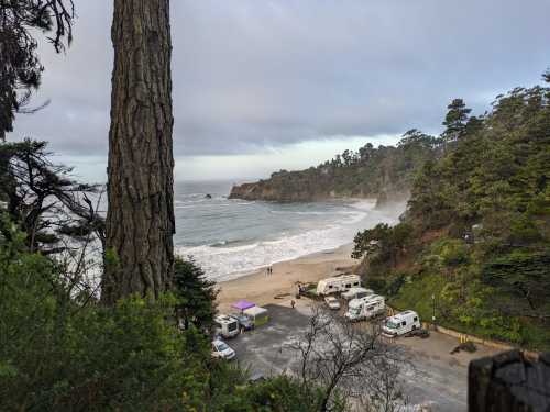 A scenic beach view with RVs parked, surrounded by trees and misty cliffs under a cloudy sky.