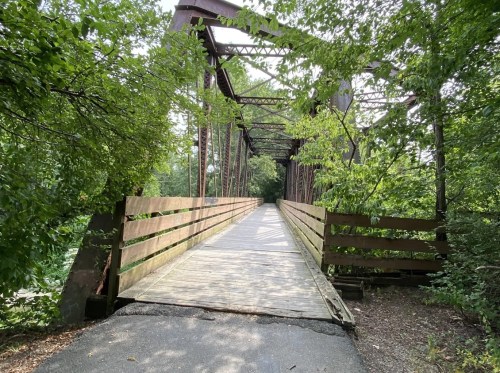 A weathered metal bridge surrounded by lush greenery, leading into a serene, wooded area.