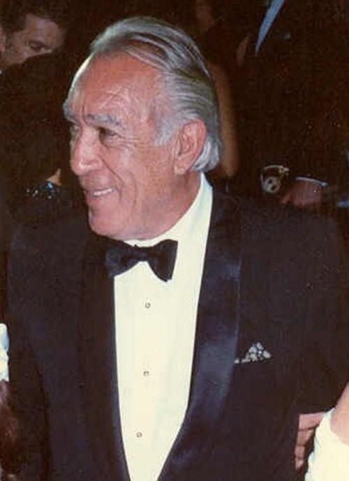 A smiling man in a tuxedo with a bow tie, attending a formal event.
