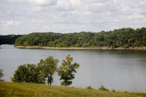 A serene lake surrounded by lush green trees under a partly cloudy sky.
