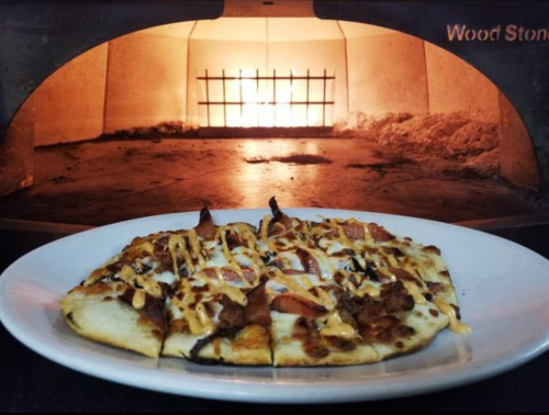 A freshly baked pizza on a plate, with a wood-fired oven glowing in the background.