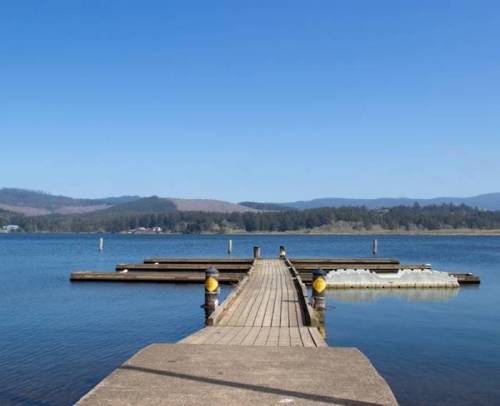 A wooden dock extends into a calm lake, surrounded by mountains under a clear blue sky.