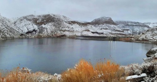A serene lake surrounded by snow-covered hills and autumn foliage under a cloudy sky.