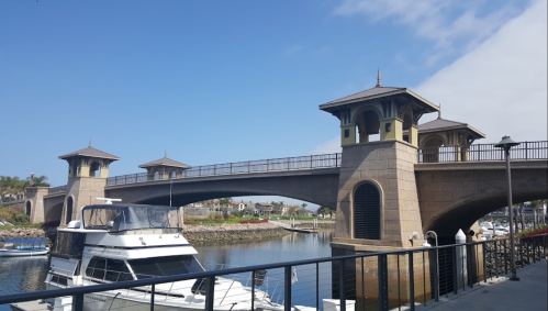 A scenic view of a bridge with towers over a marina, featuring boats and clear blue skies.