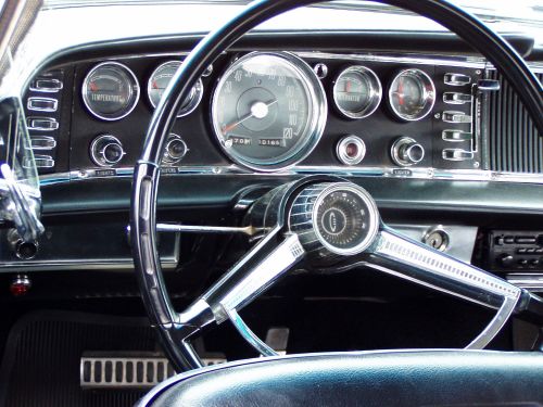 Close-up of a vintage car dashboard featuring a steering wheel, gauges, and chrome accents.