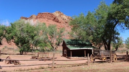 A rustic wooden cabin surrounded by trees and a red rock formation under a clear blue sky.