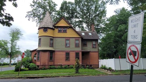A colorful Victorian-style house with a turret, surrounded by trees, next to a street sign indicating a weight limit.