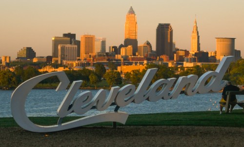Cleveland skyline at sunset with a large "Cleveland" sign in the foreground.