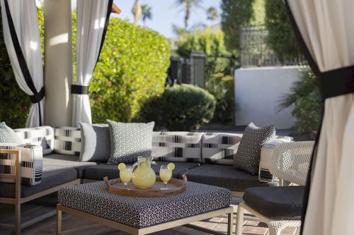 A stylish outdoor lounge area with a sectional sofa, decorative pillows, and a tray of drinks on a coffee table.